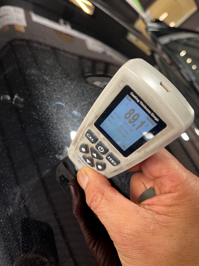Paint-thickness gauge showing about 89 microns on a metallic-black Outlander bonnet